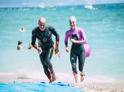 Due nuotatori in muta che escono dal mare sorridendo